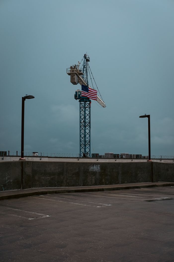 Tall construction crane displaying the American flag at a city rooftop construction site.
