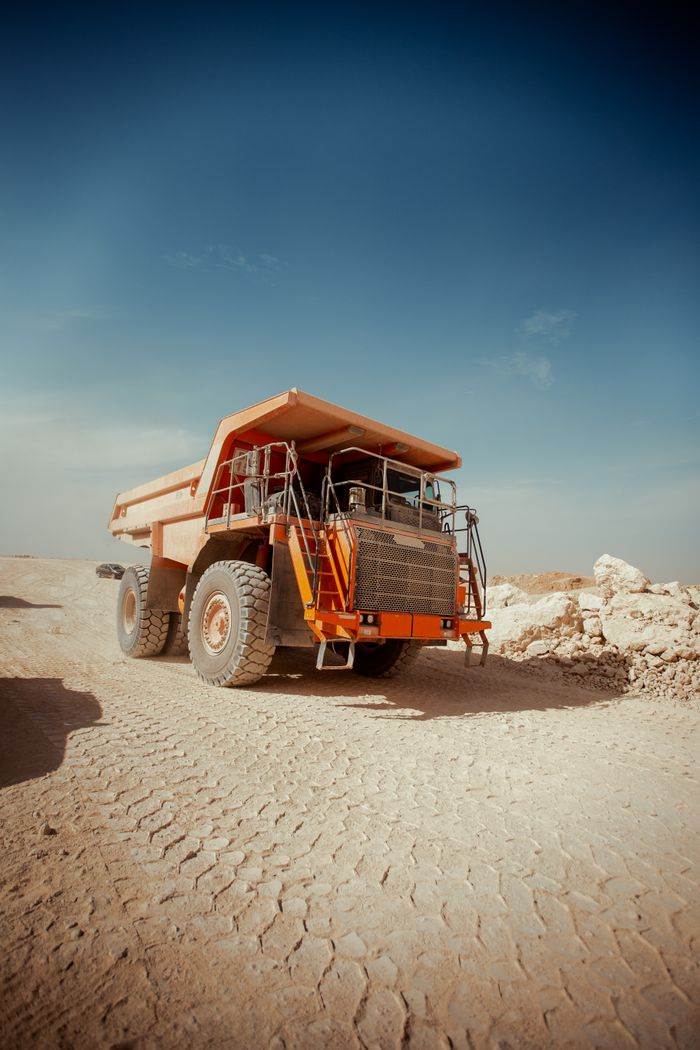 Massive dump truck on a dusty road in Texas City desert, clear sky above.