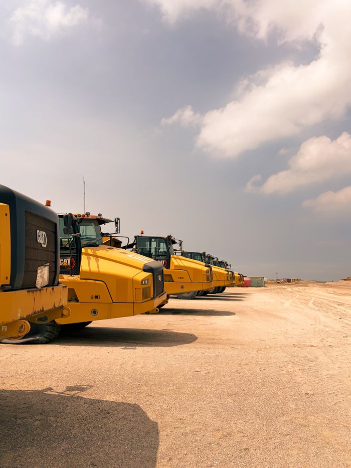 Yellow construction vehicles aligned on a dusty construction site under a cloudy sky.